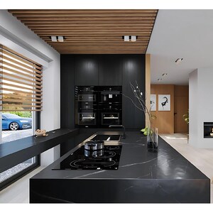 Pu&ograve; includere: Una cucina moderna con una grande isola in marmo nero con piano cottura a induzione integrato, mobili nero opaco e un soffitto a listelli di legno. Un lungo bancone nero corre lungo la finestra e si vede una zona pranzo con sedie bianche.