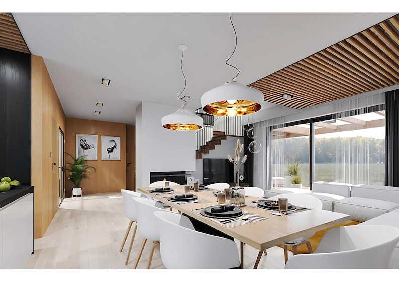 Pu&ograve; includere: Una sala da pranzo con un lungo tavolo in legno e sedie bianche, due lampade a sospensione bianche con interno dorato e una grande finestra. Lo spazio presenta pavimenti in legno chiaro, accenti neri e una scala sullo sfondo.