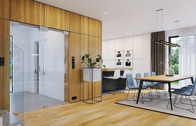 May include: A modern interior space featuring a glass door with metal hardware set into a light wood paneled wall, a white planter on a black metal stand, a wooden dining table with blue chairs, and a kitchen area with white cabinetry.