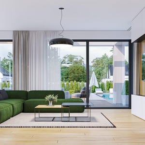 May include: A large, L-shaped forest green sectional sofa sits on a light-colored area rug in a bright living room. The space features light wood flooring, a low-profile rectangular coffee table, a black pendant light, and a white media wall.