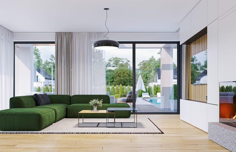 May include: A large, L-shaped forest green sectional sofa sits on a light-colored area rug in a bright living room. The space features light wood flooring, a low-profile rectangular coffee table, a black pendant light, and a white media wall.