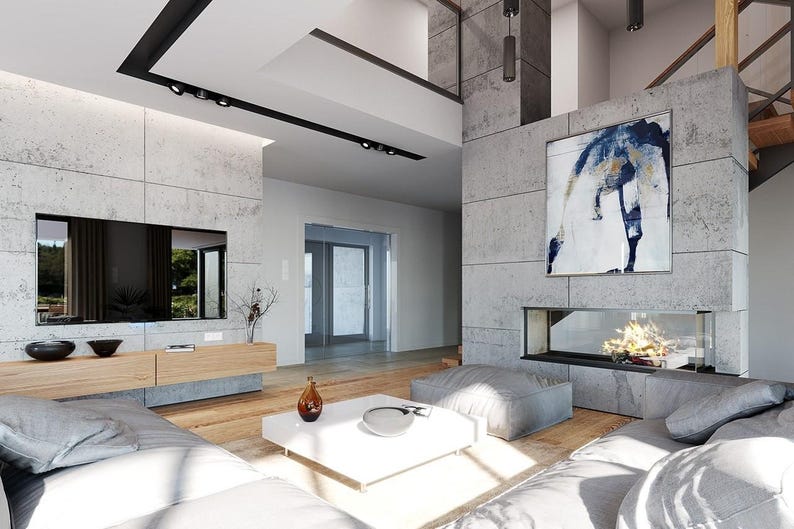 May include: A living room featuring a flat-screen television mounted on a concrete wall, a light wood media console, a white square coffee table, gray floor cushions, and a fireplace integrated into a large concrete pillar with abstract art.