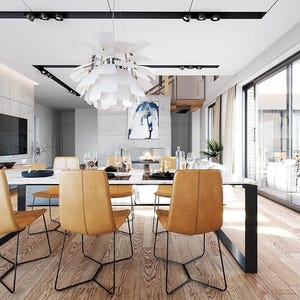 May include: A dining room featuring a white rectangular table with black metal legs, surrounded by six tan leather chairs with thin black metal frames. A large white multi-layered pendant light hangs above the table, and a television is mounted on a concrete wall.