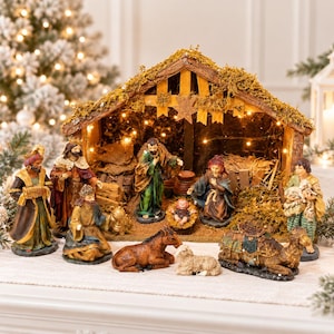 May include: A nativity scene set featuring a wooden stable structure with moss accents and internal string lights. The set includes figurines of the holy family, three wise men, a shepherd with a lamb, a camel, a donkey, and a sheep.