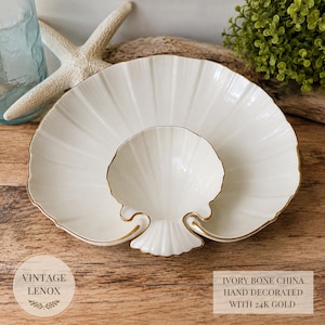 May include: An ivory bone china serving dish shaped like a large scallop shell with a smaller shell-shaped compartment in the center. The edges of the dish are trimmed with 24k gold. The text on the image reads VINTAGE LENOX and IVORY BONE CHINA HAND DECORATED WITH 24K GOLD.
