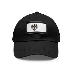 May include: A black baseball cap with a white patch featuring a black eagle with a gold crown on a white background.