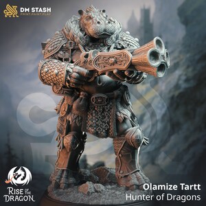 May include: A gray, detailed miniature figurine of a hippopotamus-like creature wearing armor and holding a multi-barreled gun. The figurine is standing on a base with the text "Rise of the Dragon" and "Olamize Tartt Hunter of Dragons".