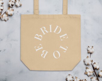 May include: A beige tote bag with white text that reads "Bride to Be" in a circle.