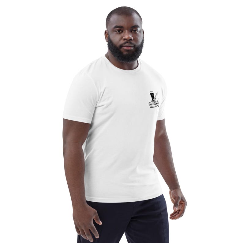 May include: White short-sleeve t-shirt with a small black graphic on the chest. The graphic appears to be a stylized image of a cocktail being prepared. The shirt is made of a soft material.