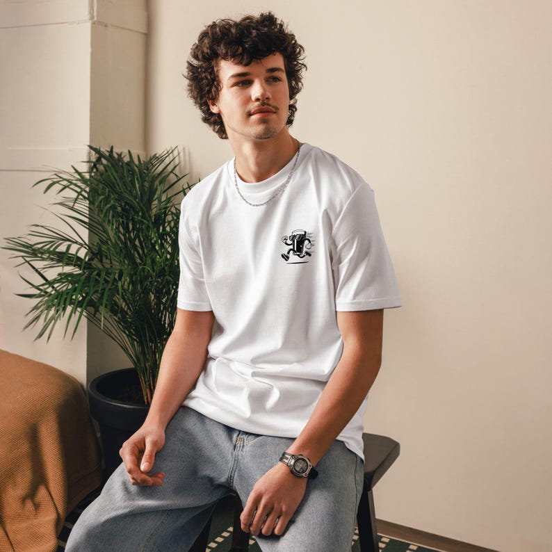 May include: White t-shirt with a small black and white graphic of a running figure. The shirt is short-sleeved and appears to be made of a soft material. The person is wearing blue jeans and a watch.