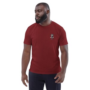 May include: A maroon short-sleeve t-shirt with a small graphic on the left chest. The graphic appears to be a stylized design in black and white. The shirt is made of a soft material.