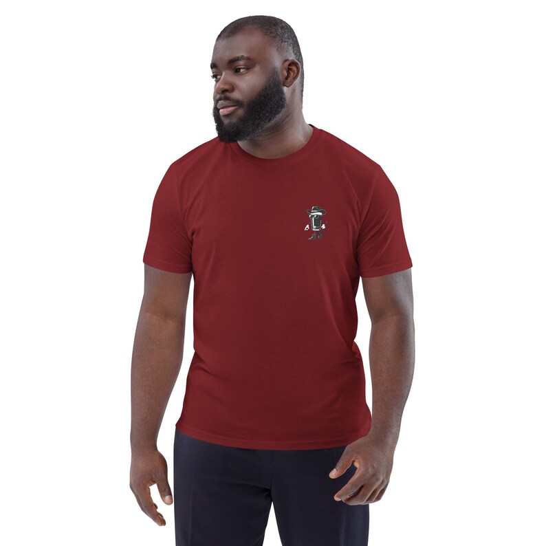 May include: A maroon short-sleeve t-shirt with a small graphic on the left chest. The graphic appears to be a stylized design in black and white. The shirt is made of a soft material.