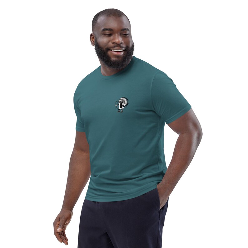 May include: Teal short-sleeve t-shirt with a small graphic on the chest. The graphic appears to be a cartoon character with a circular design. The shirt is made of a soft material and has a classic crew neck.