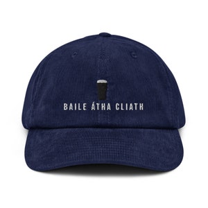May include: A navy blue corduroy baseball cap with white embroidery that reads "BAILE ÁTHA CLIATH" and a black and white illustration of a pint glass.