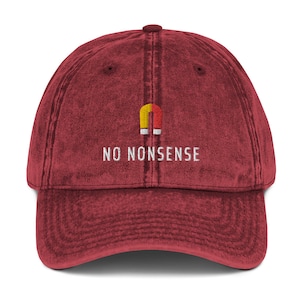 Può includere: Un berretto da baseball vintage rosso con un grafico di calamita giallo e rosso e il testo "NO NONSENSE" ricamato in bianco.