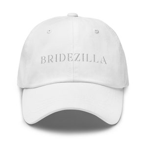 Puede incluir: Gorra de béisbol blanca con el texto "BRIDEZILLA" bordado en plata en la parte delantera.