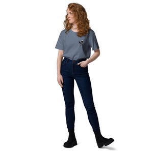 May include: A person wearing a blue t-shirt with a small black and white graphic on the chest, dark blue jeans and black boots. The t-shirt is plain, and the jeans are high-waisted.