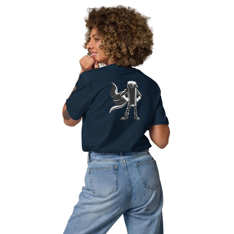 May include: A navy blue t-shirt with a white graphic of a superhero-like object and cape on the back. The person in the image is wearing light blue jeans. The t-shirt is a dark blue color.