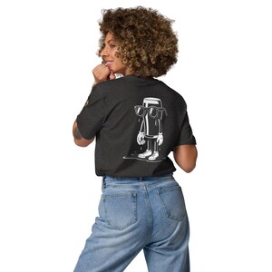 K&ouml;nnte beinhalten: Dunkelgraues T-Shirt mit einem wei&szlig;en Cartoon-Bierglas-Charakter mit Sonnenbrille, Handschuhen und Turnschuhen. Die Grafik ist auf der R&uuml;ckseite aufgedruckt. Das T-Shirt wird mit einer blauen Jeans getragen.