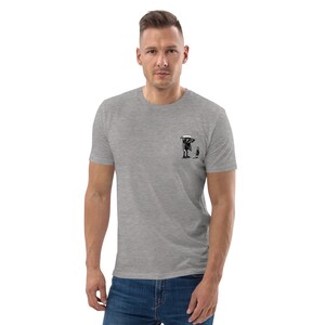 May include: A heather gray t-shirt featuring a small black graphic of a figure with a scythe and a smaller figure. The t-shirt is short-sleeved and has a crew neck. The graphic is located on the left chest area.
