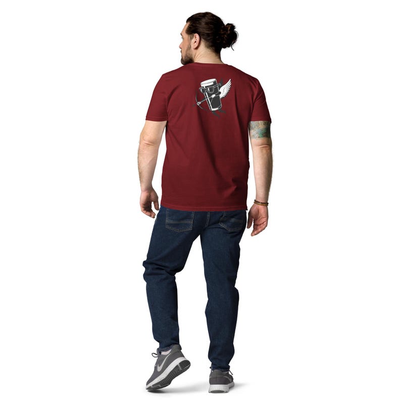 May include: A maroon t-shirt with a graphic on the back featuring a winged beer glass with a bow and arrow. The person is wearing dark blue jeans and gray sneakers.