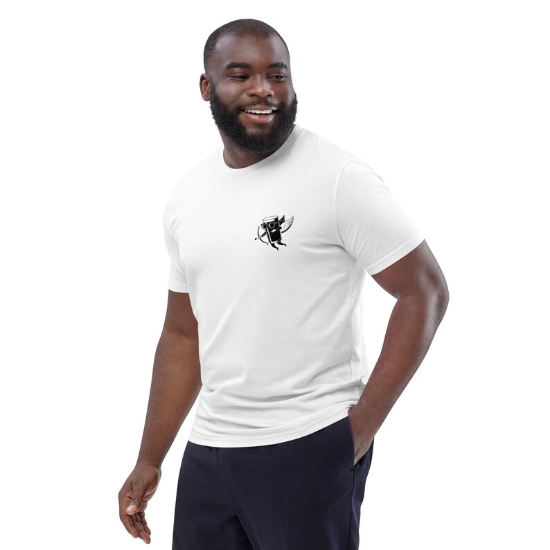 May include: White t-shirt with a small black graphic of a winged figure holding a bow and arrow. The t-shirt is short-sleeved and has a crew neck. The person is wearing navy blue pants.