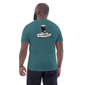 May include: Teal short-sleeve t-shirt featuring a black and white illustration of a beer glass fishing from a boat. The graphic shows the beer glass wearing sunglasses and holding a fishing rod. The shirt is made of a soft material.