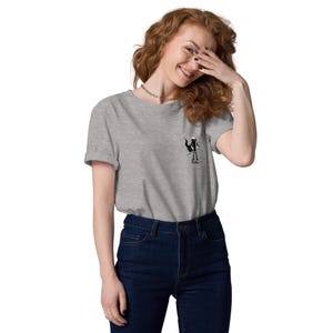 Puede incluir: Una camiseta gris jaspeado con un peque&ntilde;o gr&aacute;fico en blanco y negro en el pecho. El gr&aacute;fico parece ser una figura estilizada. La camiseta se combina con vaqueros azul oscuro.