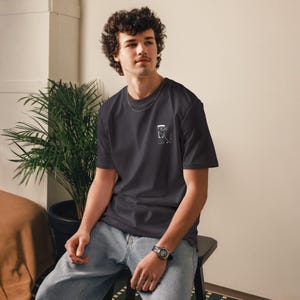 May include: Dark gray t-shirt with a small white graphic on the chest. The graphic appears to be a stylized image of a coffee maker. The shirt is short-sleeved and made of a soft material.