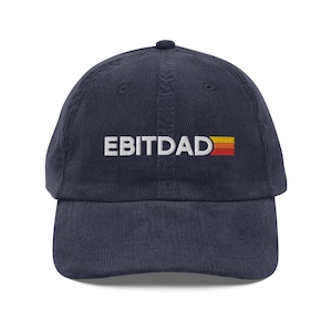 May include: A navy blue corduroy baseball cap featuring the embroidered word "EBITDAD" in white, with a retro-style orange and yellow stripe design. The cap has a curved peak and a button on top.