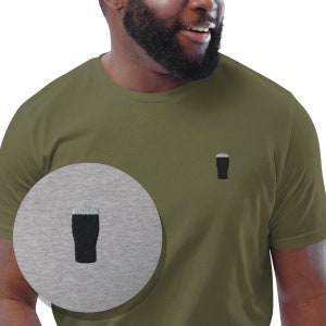 以下が含まれることがあります： 前面に黒いビールジョッキのグラフィックが描かれた緑色のTシャツ。グラフィックはグレーの背景にも表示されています。