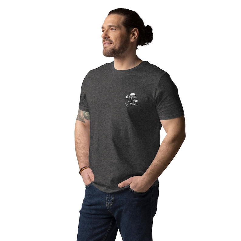 May include: Dark gray t-shirt with a small white graphic on the left chest. The graphic appears to be a stylized illustration. The shirt is made of a soft material and has short sleeves.