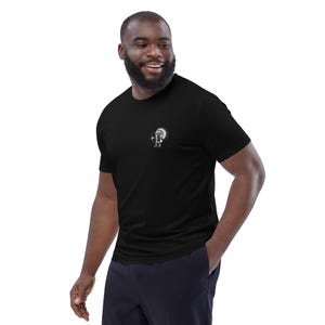 May include: Black t-shirt with a small white graphic on the chest. The graphic appears to be a stylized figure within a circular design. The t-shirt is short-sleeved and made of a soft material.