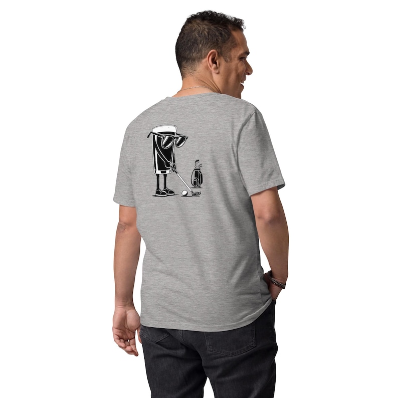 May include: A light gray t-shirt featuring a black and white graphic of a beer glass wearing sunglasses and playing golf. The design includes a golf club, ball, and golf bag. The shirt is made of a soft material.