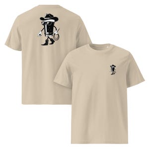 May include: Beige t-shirts with a black and white cartoon cowboy design. One shirt has the full design on the back, while the other has a smaller version on the front. The cowboy is wearing a hat, sunglasses, and boots.