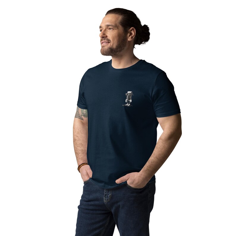 K&ouml;nnte beinhalten: Marineblaues T-Shirt mit einer kleinen schwarz-wei&szlig;en Grafik auf der Brust. Die Grafik scheint ein stilisierter Roboter oder eine Figur zu sein. Das T-Shirt besteht aus einem weichen Material und hat einen Rundhalsausschnitt.