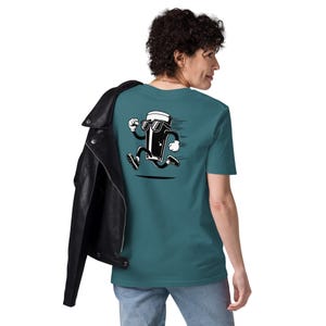 May include: Teal t-shirt featuring a cartoon pint of beer wearing sunglasses and running. The black and white graphic has motion lines. The person is wearing blue jeans and a black leather jacket.