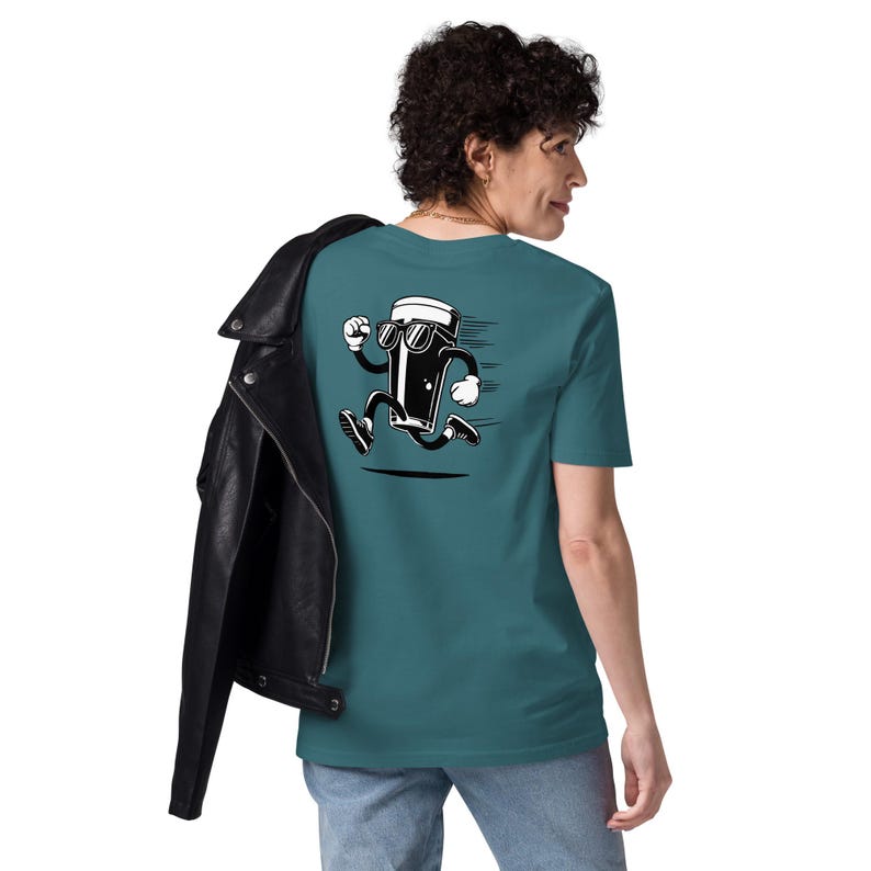 May include: Teal t-shirt featuring a cartoon pint of beer wearing sunglasses and running. The black and white graphic has motion lines. The person is wearing blue jeans and a black leather jacket.