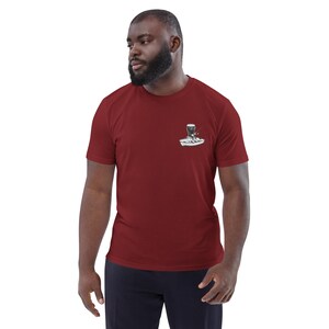 May include: Maroon short-sleeve t-shirt with a small graphic on the chest. The graphic is a black and white illustration of a boat with a person fishing. The shirt is made of a soft material.