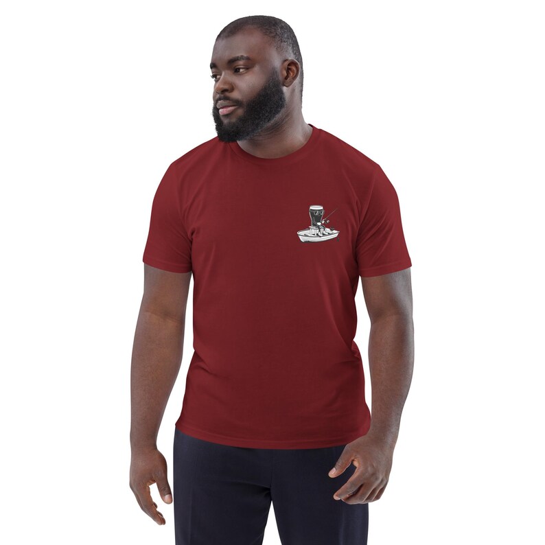 May include: Maroon short-sleeve t-shirt with a small graphic on the chest. The graphic is a black and white illustration of a boat with a person fishing. The shirt is made of a soft material.