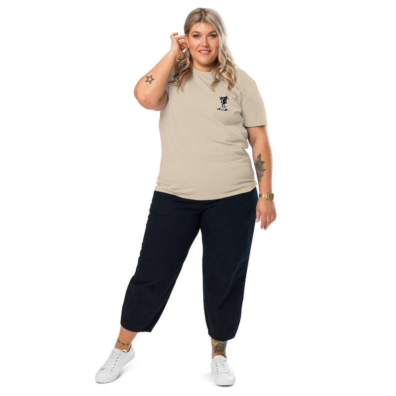 K&ouml;nnte beinhalten: Beiges T-Shirt mit kleinem schwarzem Aufdruck auf der Brust, kombiniert mit dunkelblauen, cropped Hosen und wei&szlig;en Turnschuhen. Die Person tr&auml;gt eine goldene Uhr.