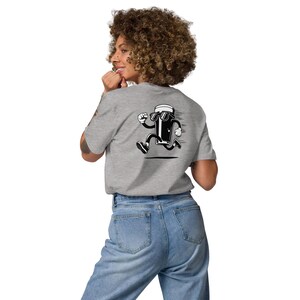 May include: A light gray t-shirt featuring a cartoon image of a running beer mug wearing sunglasses. The graphic is in black and white. The person is wearing blue jeans.