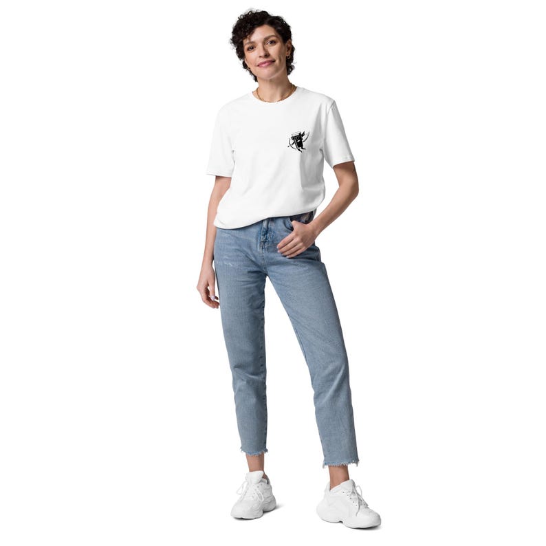 May include: White t-shirt with a small black graphic on the chest, paired with light blue jeans and white sneakers. The jeans have a straight leg cut and a raw hem. The person is wearing a casual outfit.