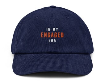 May include: A navy blue corduroy baseball cap with white embroidery that reads "In My Engaged Era" in orange lettering.