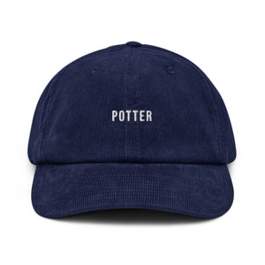 Op de afbeelding: Een donkerblauwe corduroy baseballpet met het woord "POTTER" in wit geborduurd op de voorkant.