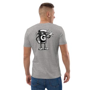 Puede incluir: Una camiseta gris con un dibujo animado de un vaso de l&iacute;quido con gafas de sol y haciendo una se&ntilde;al de aprobaci&oacute;n. El vaso tiene la letra "G" en &eacute;l. El gr&aacute;fico es en blanco y negro.