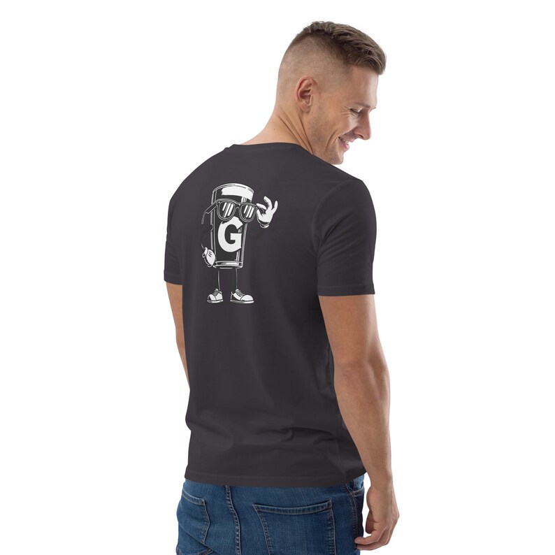 Puede incluir: Camiseta gris oscuro con un dibujo animado blanco en la espalda. El dibujo representa un personaje de taza de caf&eacute; con gafas de sol haciendo el gesto de "ok". La letra "G" es visible en la taza.