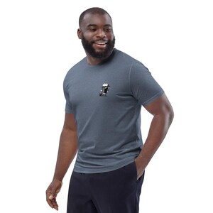 Puede incluir: Una camiseta azul jaspeado con un peque&ntilde;o gr&aacute;fico de una jarra de cerveza con patas. La camiseta de manga corta est&aacute; hecha de un material suave y la lleva una persona. La persona sonr&iacute;e y tiene barba.