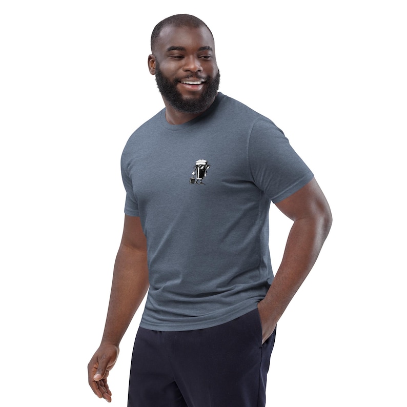 Puede incluir: Una camiseta azul jaspeado con un peque&ntilde;o gr&aacute;fico de una jarra de cerveza con patas. La camiseta de manga corta est&aacute; hecha de un material suave y la lleva una persona. La persona sonr&iacute;e y tiene barba.