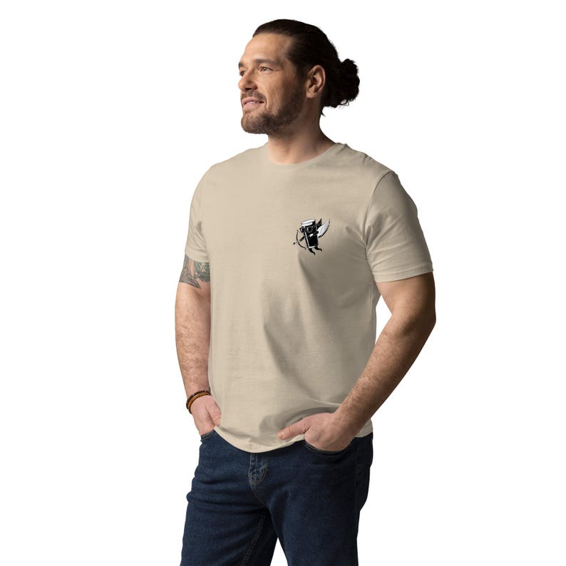 May include: Beige t-shirt with a small black and white graphic on the chest. The graphic appears to be a stylized image of a beer mug with wings and a bow and arrow. The shirt is made of a soft material.